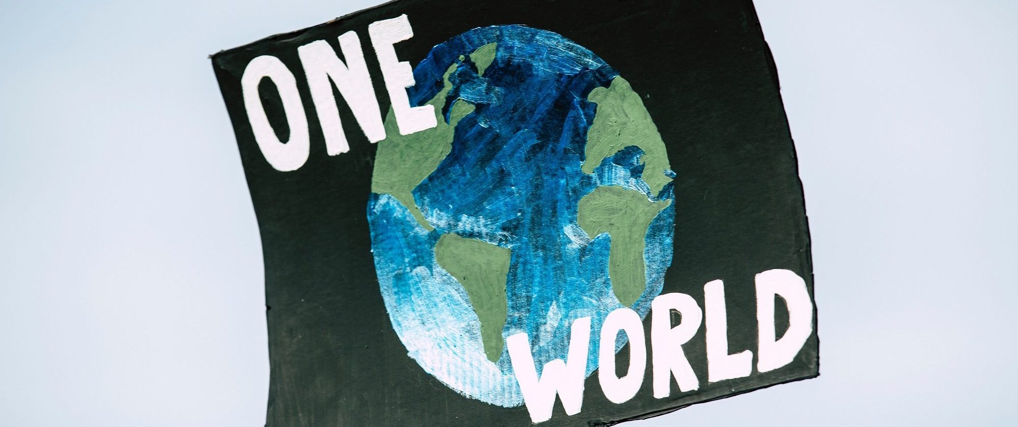 Auf einem Pappschild ist der Erdglobus gemacht. Darüber steht: One World".