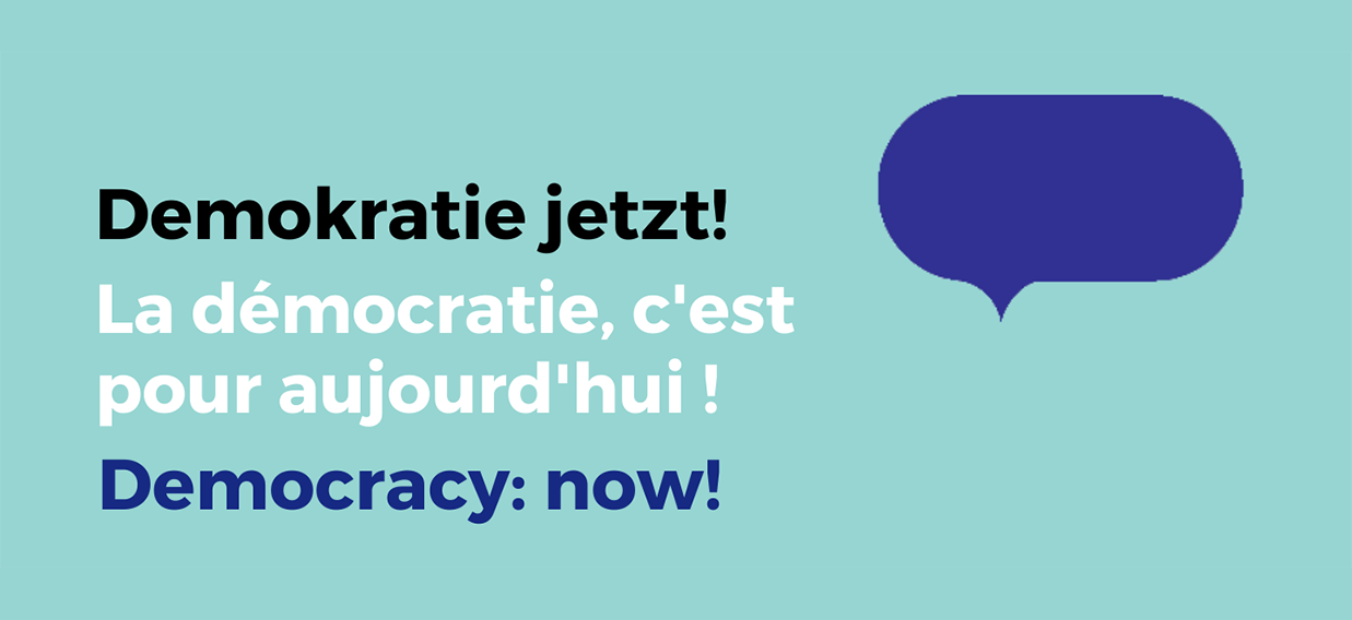 Auf blauem Grund steht "Demokratie jetzt! in Deutsch, Englisch und Französisch.