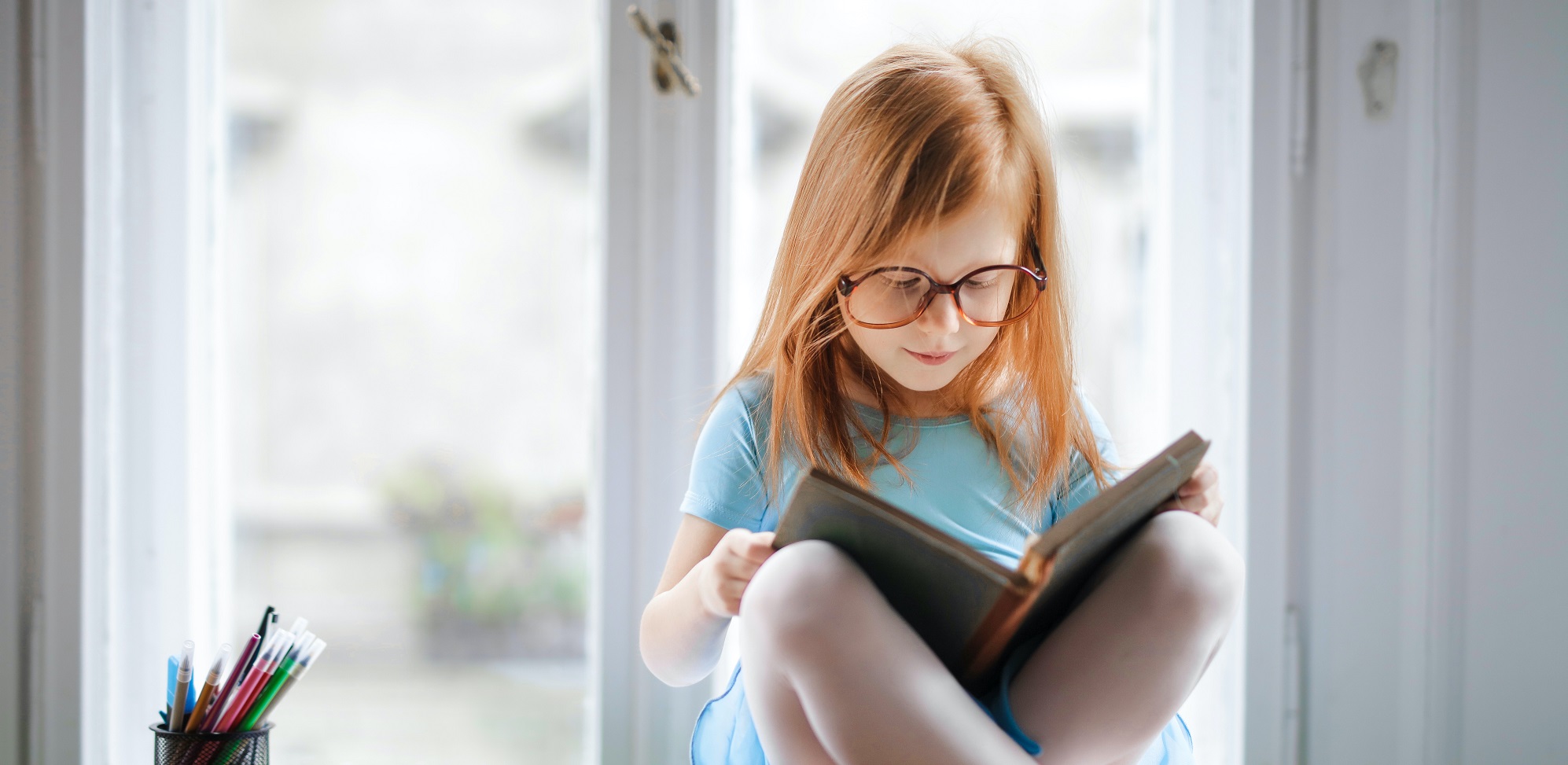 Ein Kind sitzt vor einem Fenster und liest etwas.