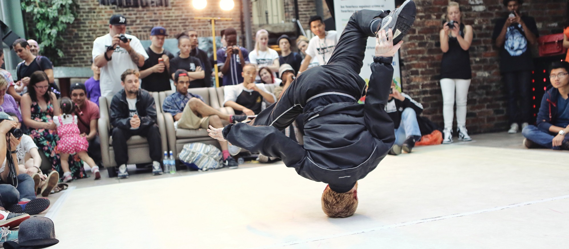 Ein junger Mensch macht einen Headspin / Breakdancemove vor diversem Publikum.