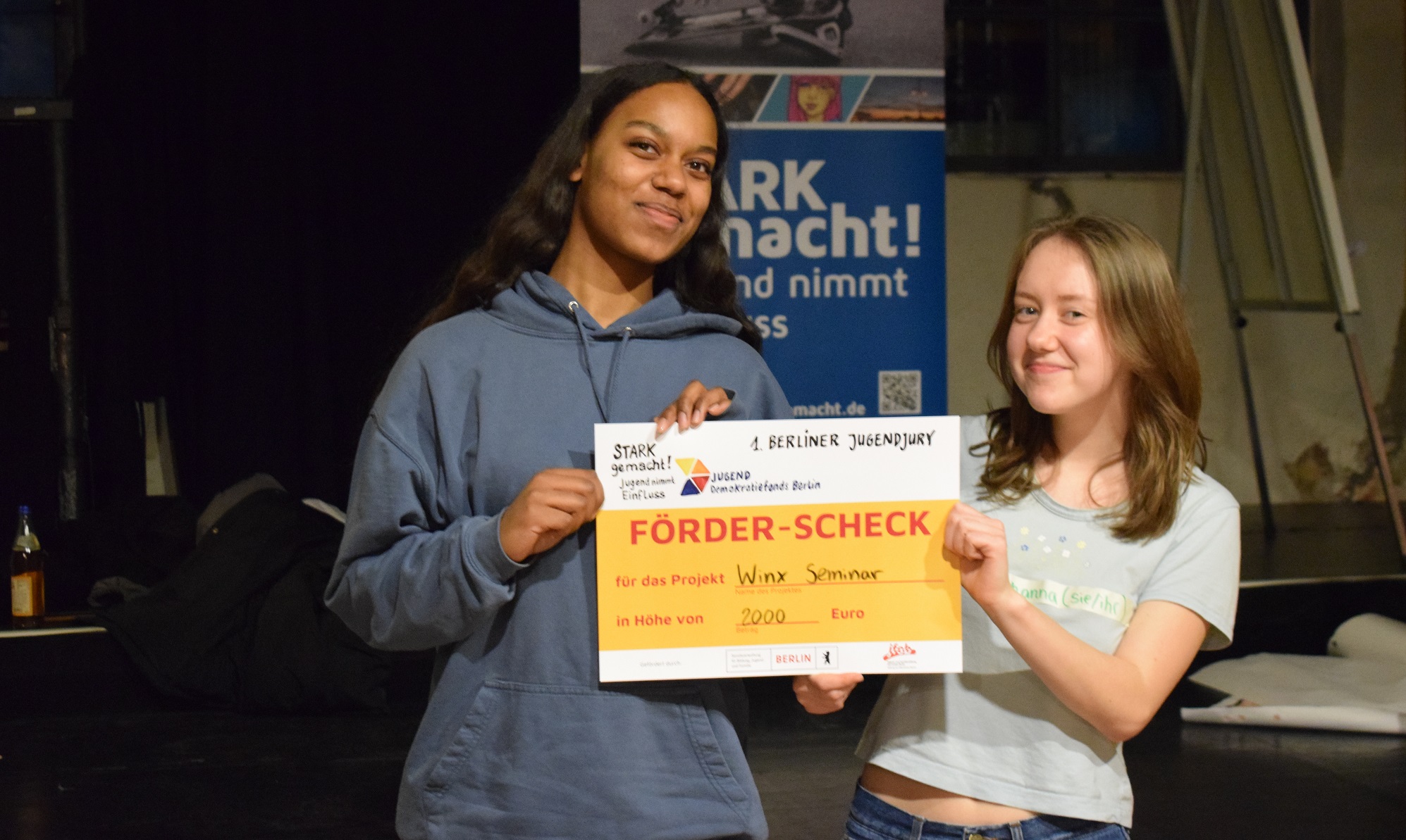 Zwei junge Menschen halten den Check für das Projekt "Winx Seminar" in den Händen
