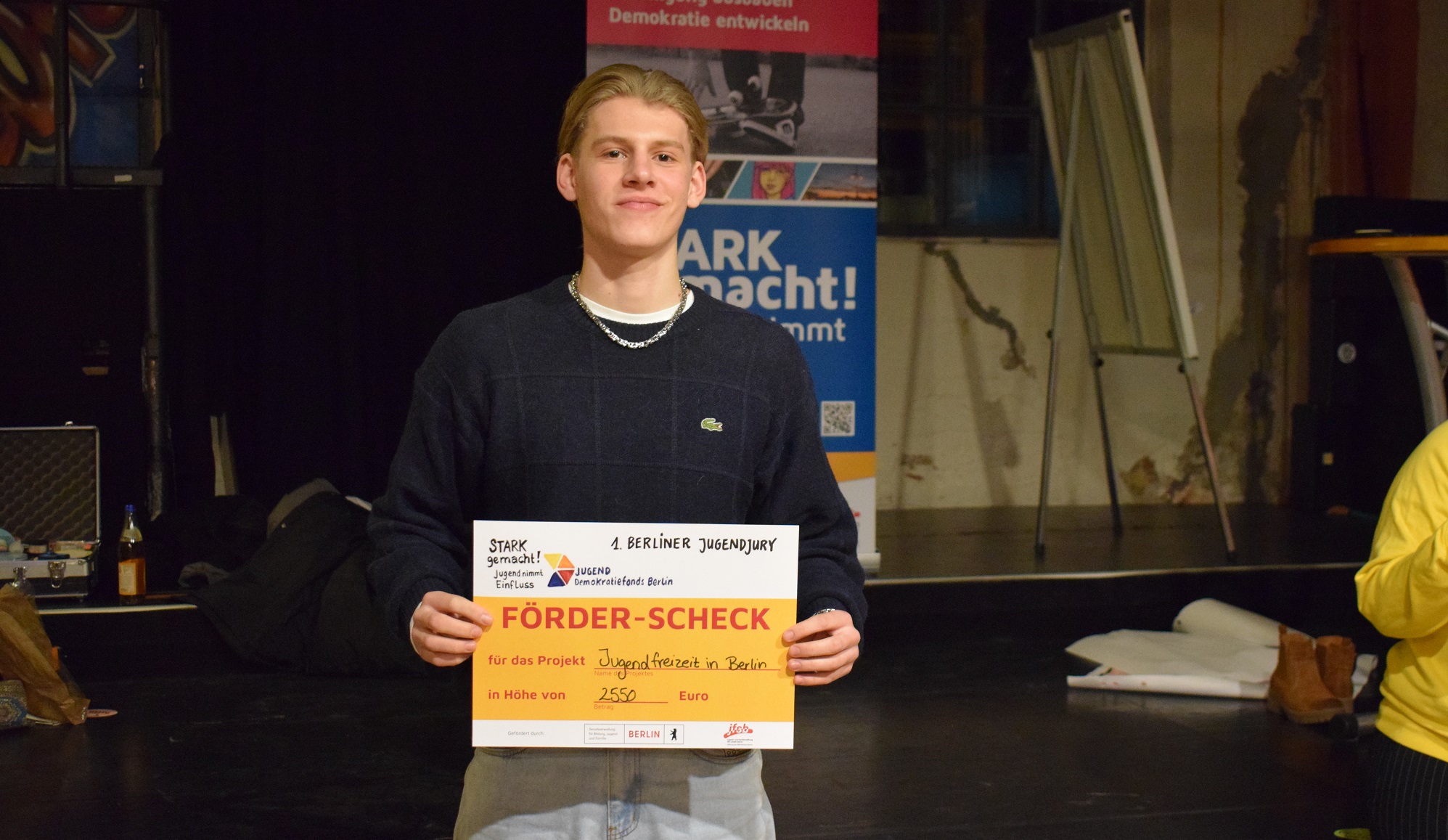 Ein junger Mensch hält den Check für das Projekt "Jugendfreizeit in Berlin" in den Händen