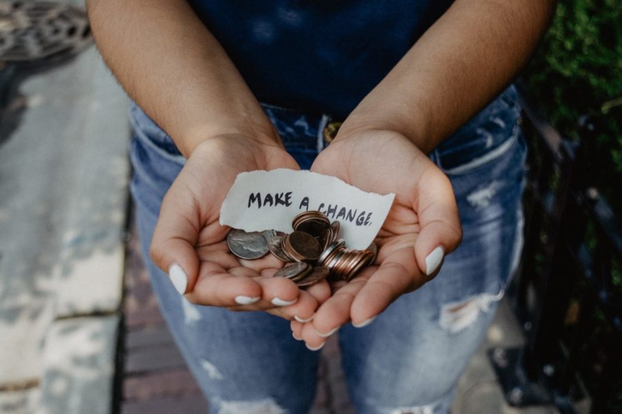 Person hält Geld in den Händen, dabei ein Zettel mit der Aufschrift "Make a change" (zu dt.: "Verändere etwas")